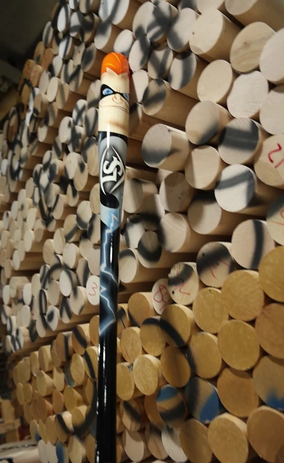 Full-length Syndrome bat leaning against a wall of raw maple billets