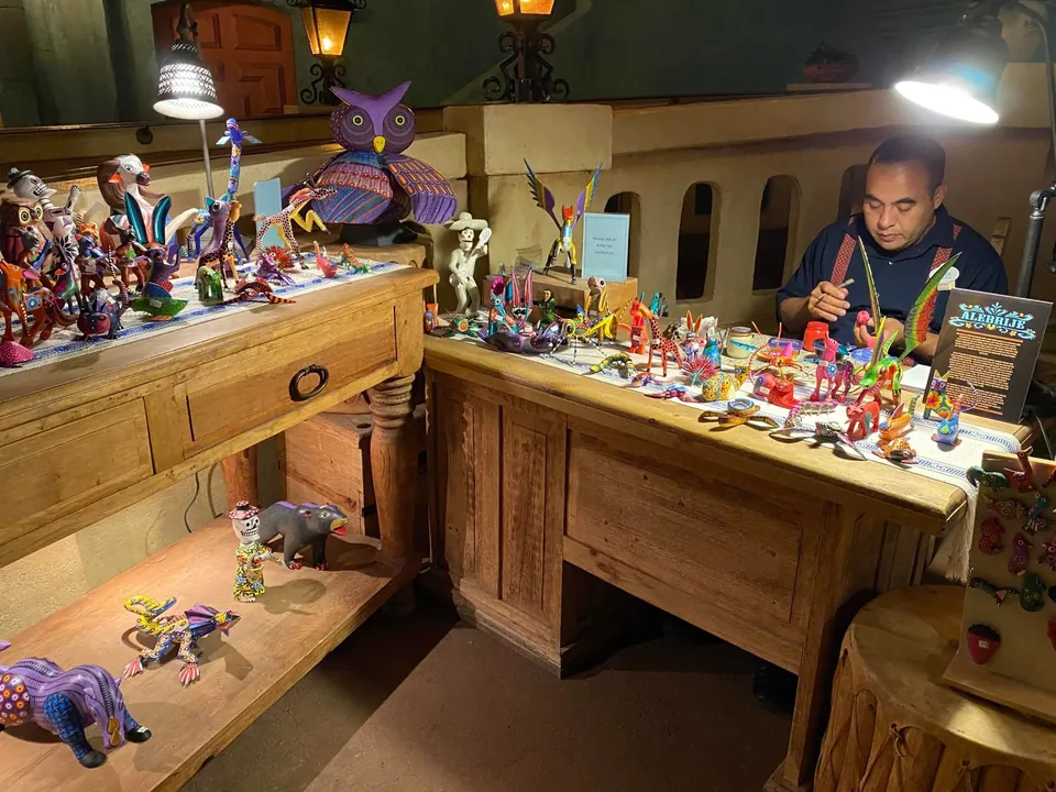 A carver at work beside a display of alebrije carvings in the EPCOT Mexico pavilion